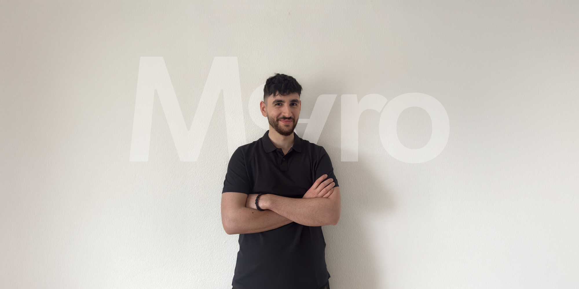 Selbstbewusstes Portrait des Movaro-Gründers in schwarzem Polohemd vor heller Wand mit Logo Hintergrund